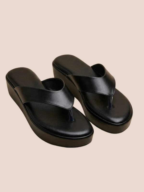 Black sandals worn with light-colored pants on a beige background.