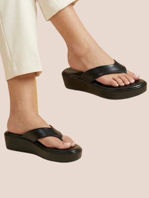 Black sandals worn with light-colored pants on a beige background.