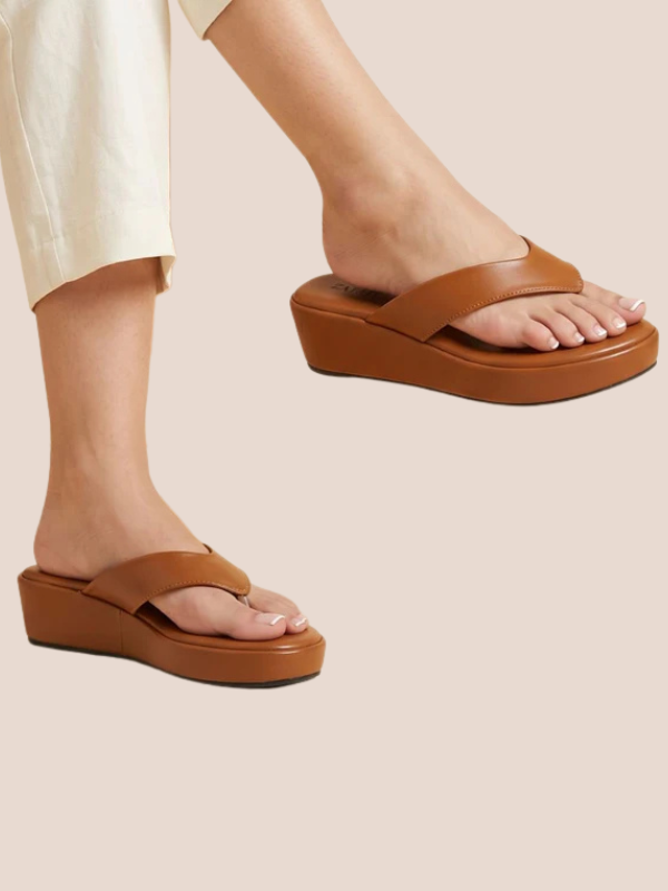 Brown sandals worn with light-colored pants on a beige background.