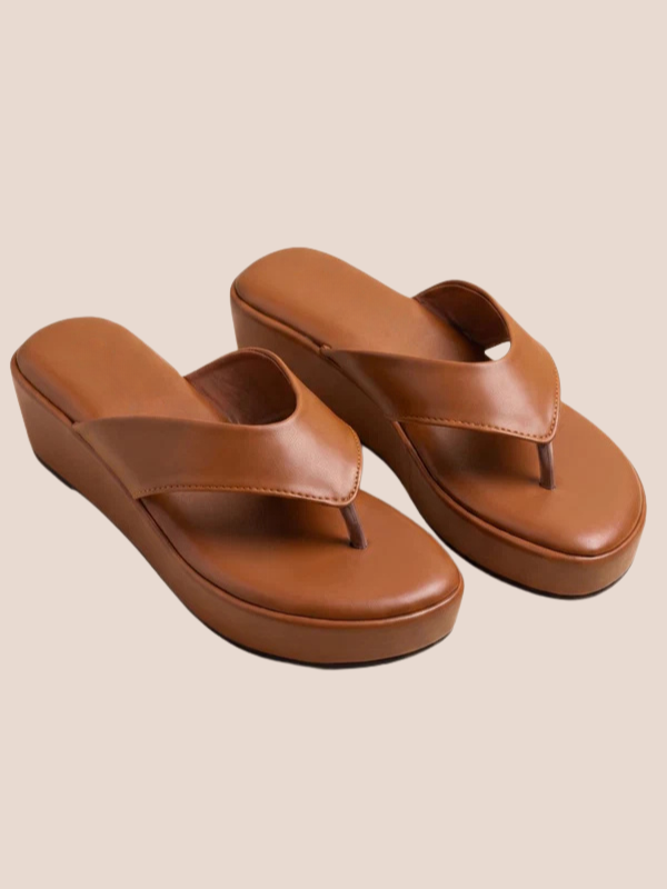 Brown sandals worn with light-colored pants on a beige background.