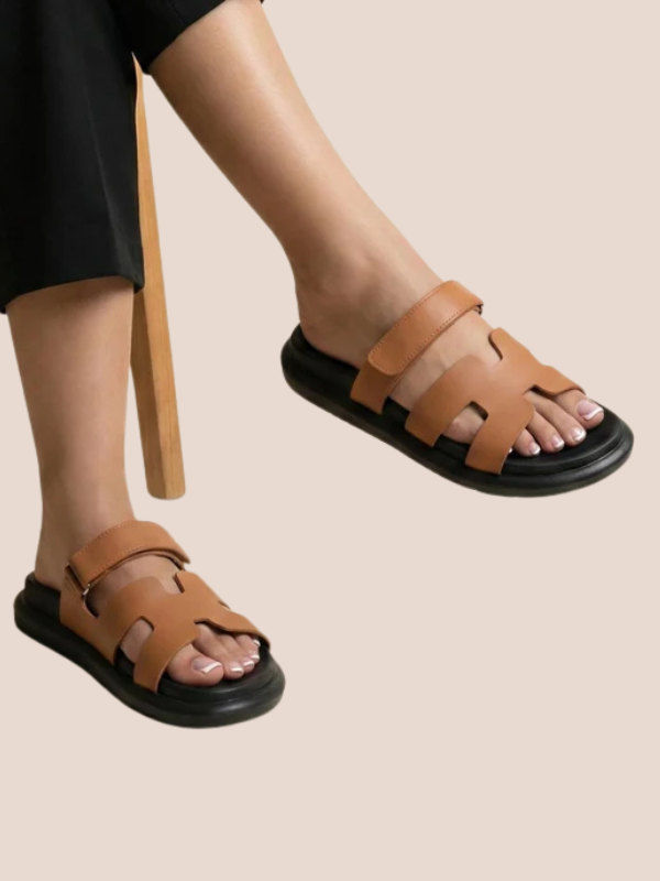 Brown Soft Stride with black soles worn by a person on a beige background.
