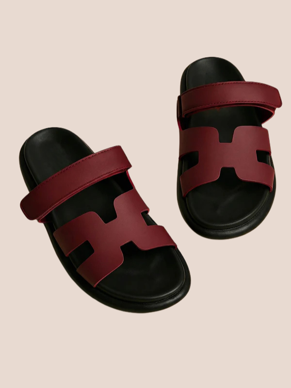 Maroon sandals with black soles worn by a person on a beige background.