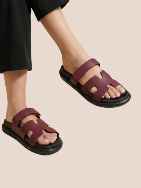Maroon sandals with black soles worn by a person on a beige background.