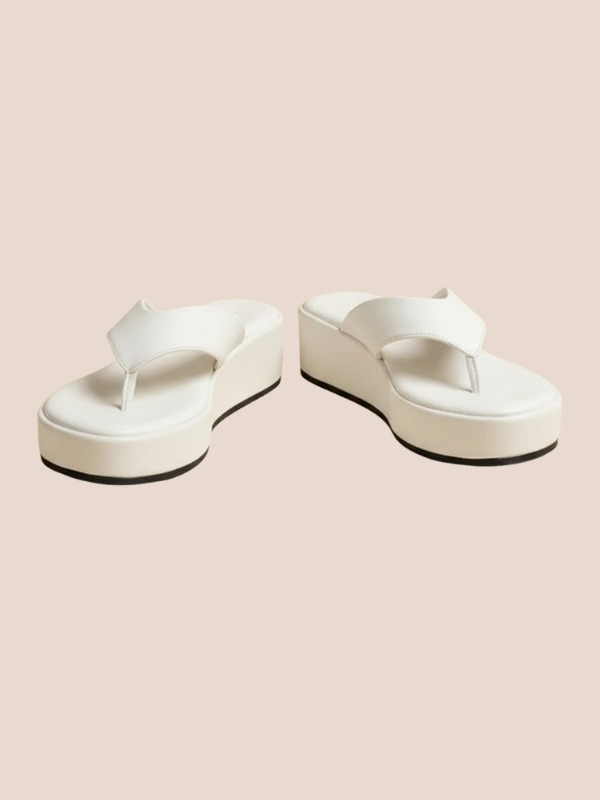White platform sandals worn by a person on a beige background.