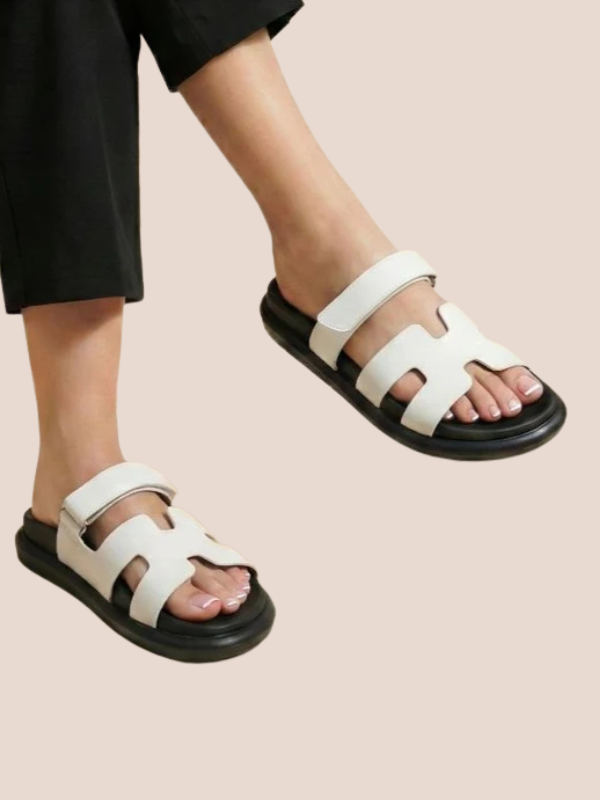 White Soft Stride with black soles worn by a person on a beige background.
